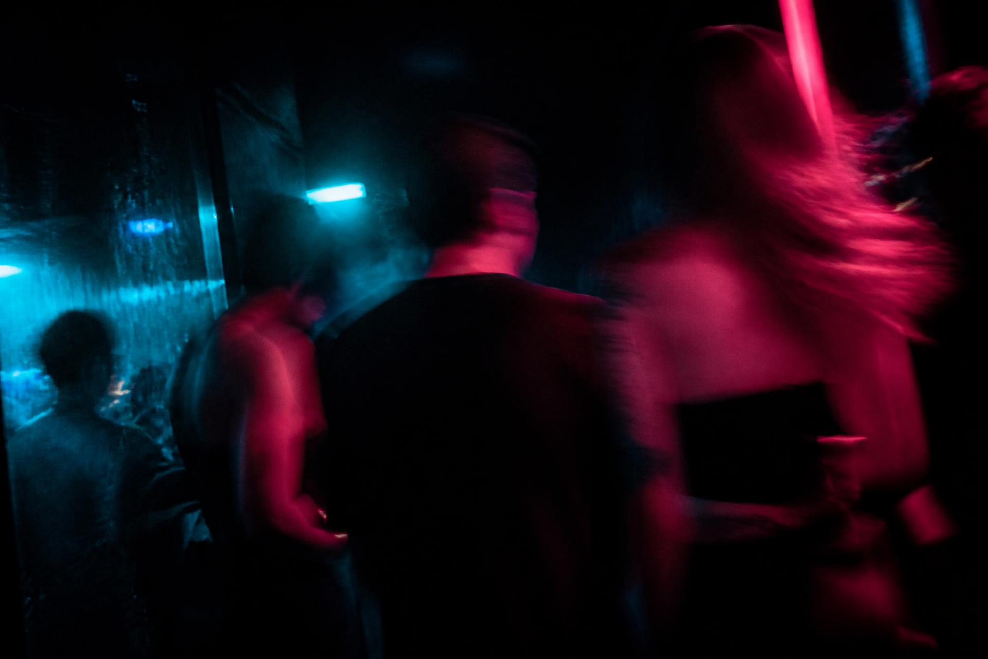 Blurred strangers moving through a nightclub lit in cyan and pink