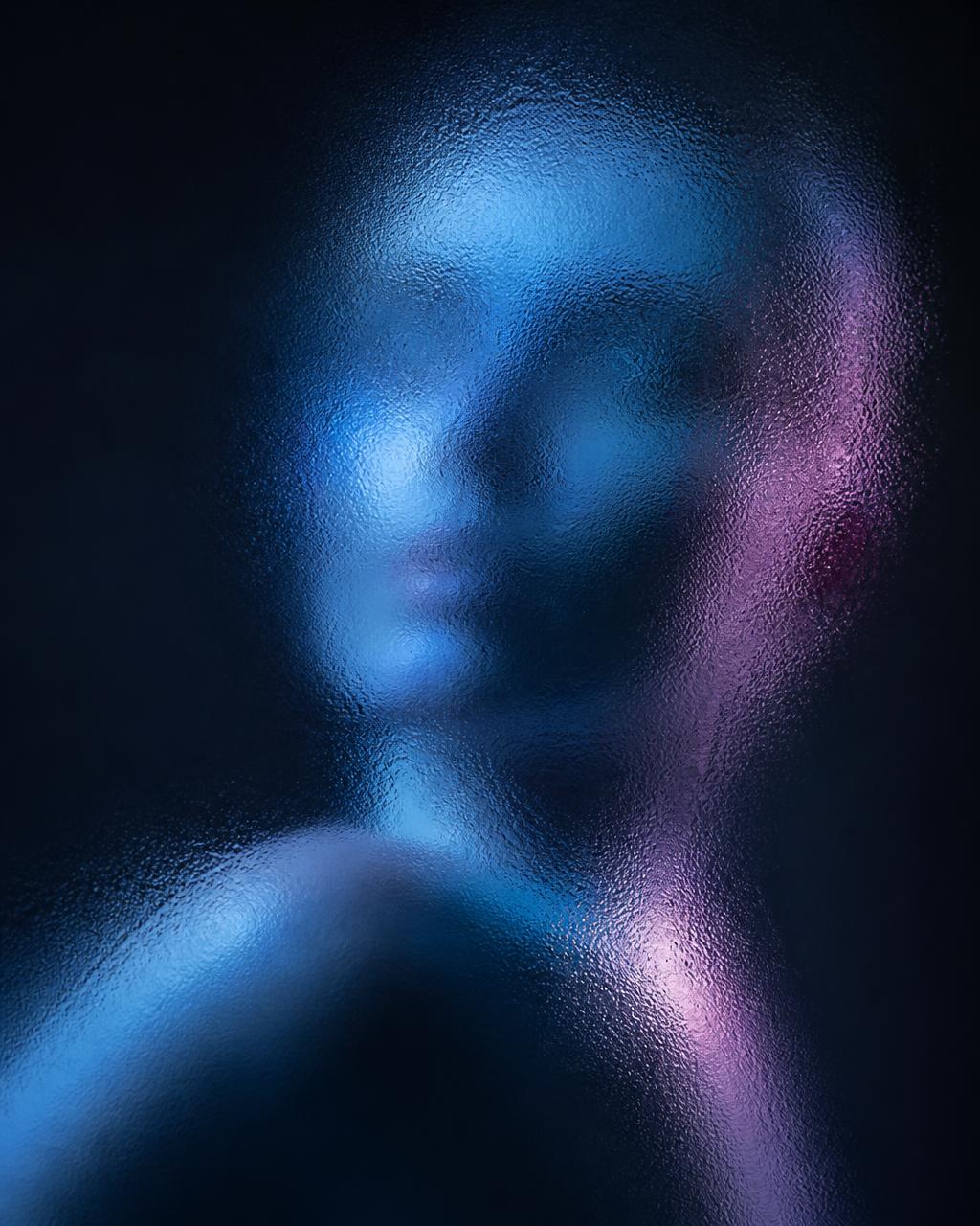 A face diffused behind frosted glass, lit in ice blue