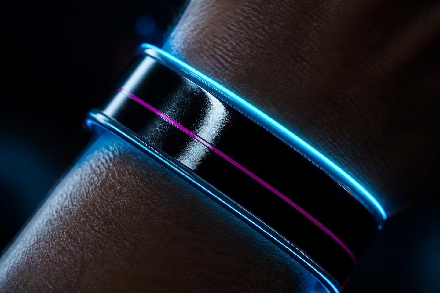 A glossy black club wristband glowing cyan with one pink stripe